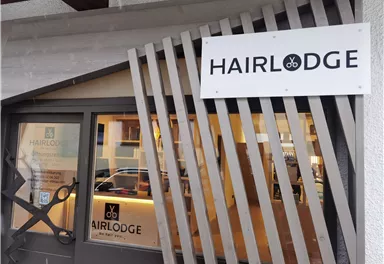 Ein Friseursalon namens "HAIRLODGE" mit einem modernen und einladenden Eingang. Die Fenster zeigen eine freundliche Atmosphäre und eine klare Beschilderung.