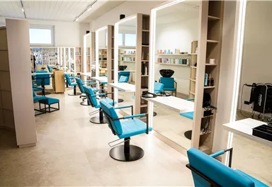 Ein moderner Friseursalon mit blauen Stühlen und großen Spiegeln. Die Regale im Hintergrund sind mit Haarpflegeprodukten gefüllt.