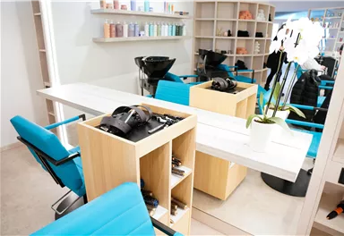 Ein modernes Friseurstudio mit stilvollen blauen Stühlen und einem hellen, minimalistischen Design. Die Regale im Hintergrund sind mit Pflegeprodukten gefüllt.