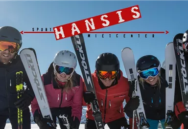 Eine Gruppe von fünf Skifahrern lächelt in der Sonne. Im Hintergrund ist ein klarer blauer Himmel zu sehen.