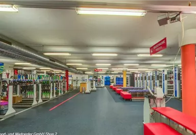 Ein modernes Fitnessstudio mit verschiedenen Trainingsgeräten und einem offenen Raum. Bänke und Geräte sind ordentlich angeordnet, bereit für das Training.