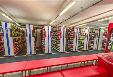 Ein Verkaufsraum mit Regalen, die verschiedene Produkte präsentieren. In der Mitte gibt es rote Sitzmöbel für Kunden.