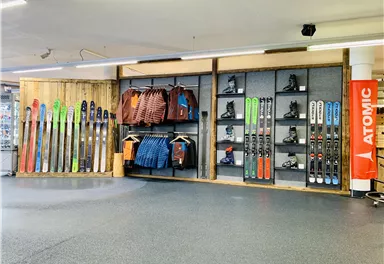 Ein Skiverleih mit einer Auswahl an Skiern, Snowboards und Bekleidung. Die Wände sind gut organisiert mit sportlicher Ausrüstung.