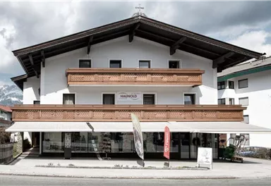 Ein modernes Gebäude im alpinen Stil mit Holzverkleidung und Balkonen. Der Himmel ist bewölkt und es gibt eine ruhige Straße vor dem Haus.