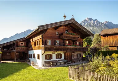 A traditional wooden house in the Alps with a well-kept garden. In the background, majestic mountains can be seen.