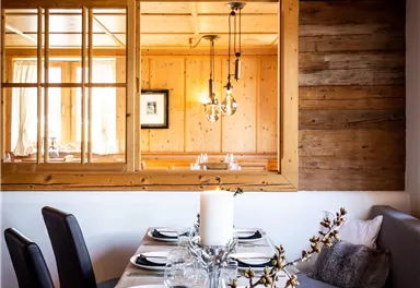 An inviting dining area with a wooden table set with dishes and glasses. In the background, cozy seating and a warm wooden ceiling can be seen.