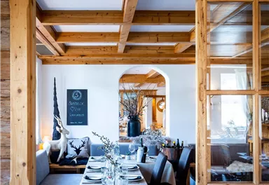 A cozy restaurant with wooden paneling and an inviting atmosphere. The tables are nicely set and visible through a large window.