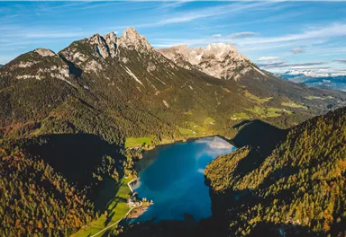 A breathtaking mountain landscape with snow-covered peaks and a clear lake in the foreground. Nature is surrounded by green forests and fields.