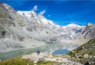 A breathtaking mountain landscape with snow-capped peaks and a clear lake. Two hikers are enjoying the view in nature.