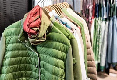 A selection of fashionable clothing, including a green jacket and various tops. The garments are neatly hanging on a rack in a store.