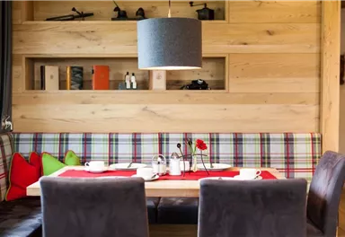 An inviting dining area with a wood-paneled background. The table is lovingly set and decorated with colorful cushions and a floral arrangement.
