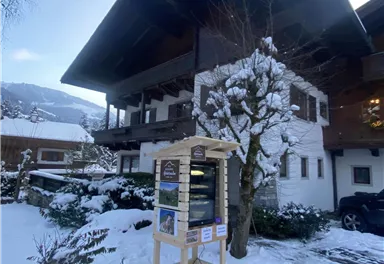 A charming house in the snow with a cozy style.  
In front of the building, there is a conference table with information.