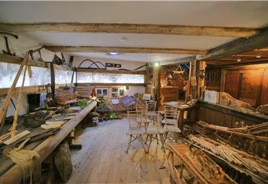 Ein traditioneller Werkraum mit Holzwerkzeugen und handgefertigten Gegenständen. Der Raum ist rustikal gestaltet und strahlt eine gemütliche Atmosphäre aus.