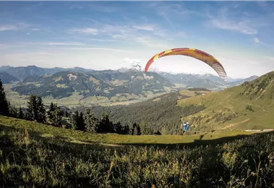 Ein Paragliding-Abenteuer in den Bergen mit herrlicher Aussicht. Der Gleitschirm schwebt über die grüne Landschaft und die sanften Hügel.