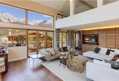 A modern living room with large windows and a view of the mountains. The decor is stylish and cozy, with a bright color scheme and wooden details.
