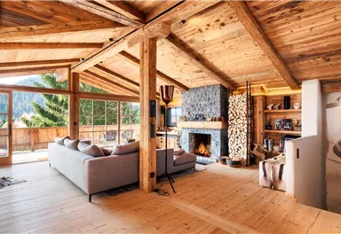 A modern wooden house with large windows and a view of nature. The cozy living area features a sofa and a fireplace that creates a warm atmosphere.