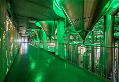 A modern interior with large, green storage tanks and metallic piping. The floor is green, and the room has an industrial atmosphere.