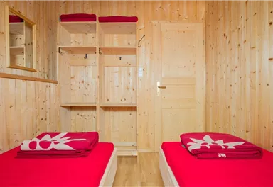 Ein gemütliches Zimmer mit zwei Einzelbetten und roten Handtüchern. Die Wände sind aus hellem Holz und es gibt einen Spiegel sowie einen Kleiderschrank.