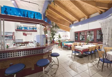 Ein einladendes Restaurant mit einem modernen Barbereich und Tischen. Das Holzdecke und die Pflanzen schaffen eine warme Atmosphäre.