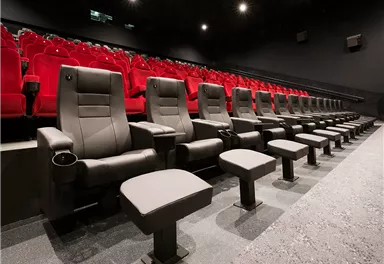 A modern cinema with comfortable black seats and red spots. The room is dark and inviting, ideal for a film experience.