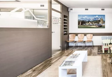 A modern waiting room with wooden flooring and beige chairs. A picture of a landscape hangs on the wall.