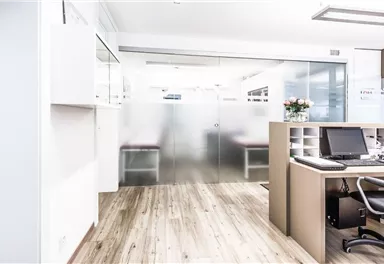 A modern office with a bright wooden floor and clear walls. The desk is decorated with a computer and plants.