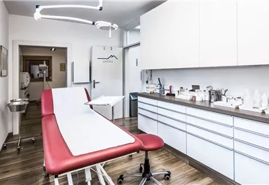 A modern treatment room with a red treatment table and a clean, tidy workspace. The walls are bright, and the room feels friendly and inviting.
