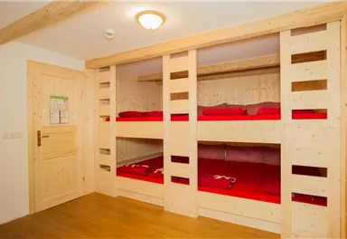 Ein Schlafzimmer mit Holzmöbeln und zwei Etagenbetten. Die Betten sind mit roten Bettwäsche ausgestattet.