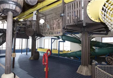 Ein Indoor-Spielplatz mit Rutschen und einem Kletterbereich. Die bunten Strukturen und das helle Licht schaffen eine freundliche Atmosphäre für Kinder.