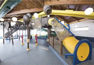 Ein Spielbereich mit Klettergerüsten und Rutschen in einem hellen Raum. Die Ausstattung besteht aus bunten Elementen, ideal für Kinder.