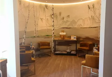 An elegant waiting area with cozy armchairs and a beautiful wall mural. Soft lighting and natural colors create a relaxing atmosphere.