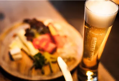 A glass of beer is next to a plate with various types of sausage and cheese. The scene is cozy and inviting.