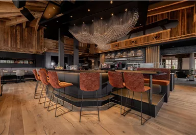 A stylish restaurant with modern wood and metal details. The well-lit bar area is furnished with elegant chairs.