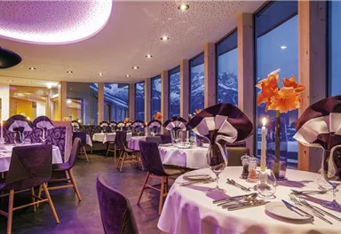 An elegant restaurant with large windows and a view of the mountains. The tables are beautifully set and decorated with flowers.
