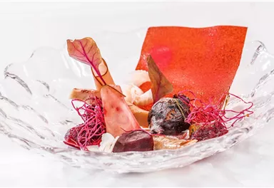 An artfully arranged dish in a glass bowl. It consists of colorful ingredients, including red and black elements as well as edible decorations.