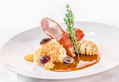 An elegant dish with roasted meat, sauerkraut, and a noodle side. The meal is artfully arranged and garnished with fresh herbs.