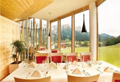An elegant restaurant with large windows and a view of the mountains. The tables are beautifully set and the decor is modern and inviting.