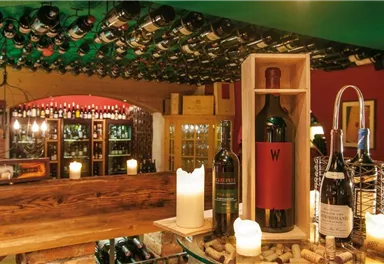 A stylish wine room with shelves full of wine bottles. In the foreground, there are various wines and candles on a wooden table.