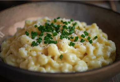A serving of creamy pasta with cheese, garnished with fresh chives. The dish is served in a rustic bowl.