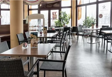Ein modernes Restaurant mit vielen Tischen und Stühlen. Große Fenster lassen viel Licht herein und es sind Pflanzen um die Räume verteilt.