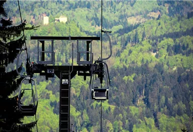 Eine Seilbahn fährt durch eine grüne Landschaft mit Bergen im Hintergrund. Die Natur ist üppig und malerisch.