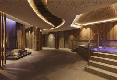 Ein eleganter Spa-Bereich mit Holzverkleidung und sanftem Licht. Eine Treppe führt zu einem Wasserbereich mit entspannender Atmosphäre.