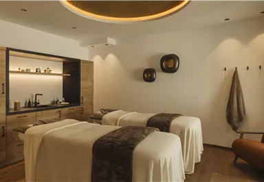 Ein elegantes Spa mit zwei Behandlungsliegen und warmen Farben. Die Einrichtung ist modern und einladend.