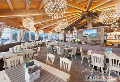 A cozy restaurant with wood decor and large windows that offer a view of the mountains. The atmosphere is inviting, with modern lighting installations and rustic furniture.
