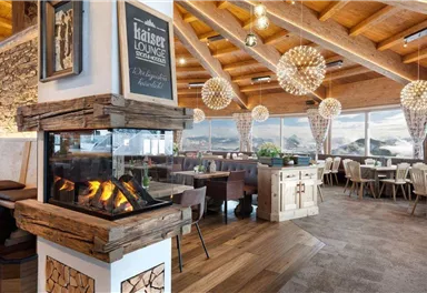 A modern restaurant with wooden decor and large windows. The fireplace creates a cozy atmosphere and offers a view of the surroundings.