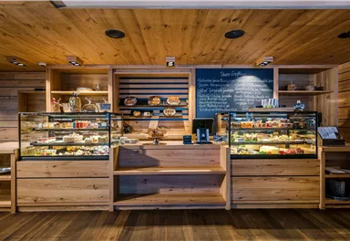 Ein gemütliches Café mit Holzmöbeln und verglasten Vitrinen. Die Vitrinen zeigen eine Auswahl an frisch gebackenem Gebäck und Snacks.