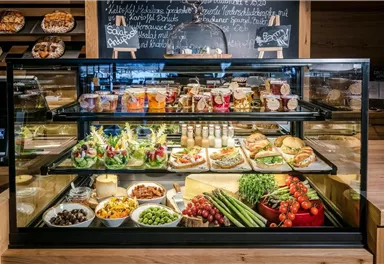 Eine ansprechende Vitrine mit verschiedenen leckeren Speisen und Snacks. Auf dem Tisch sind Salate, Sandwiches und frisches Obst zu sehen.