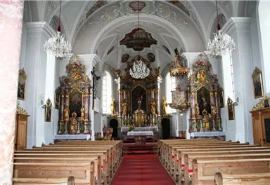 Eine prächtige Kirche mit reich verzierten Altären und einer hohen Decke. Die Holzbankreihen bieten Platz für die Gottesdienstbesucher.