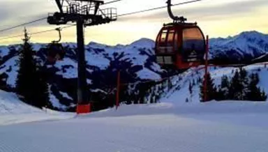 Eine Winterlandschaft mit schneebedeckten Bergen und einer Seilbahn. Der Himmel ist klar und die Piste sieht präpariert aus.