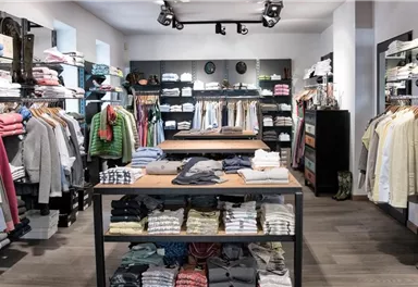 A well-organized clothing store with racks full of clothes. There are several tables with carefully folded garments.